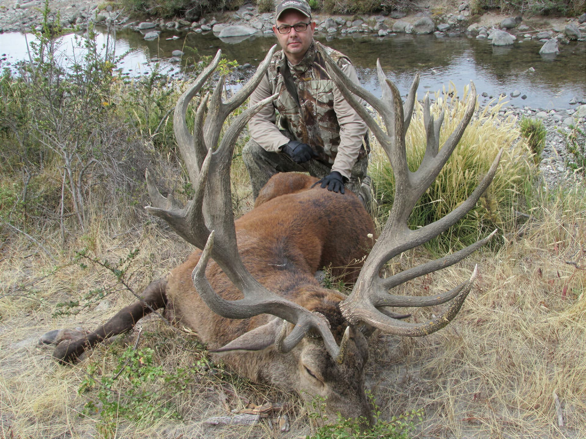 Hunter with a massive red stag on a Patagonian riverbank
