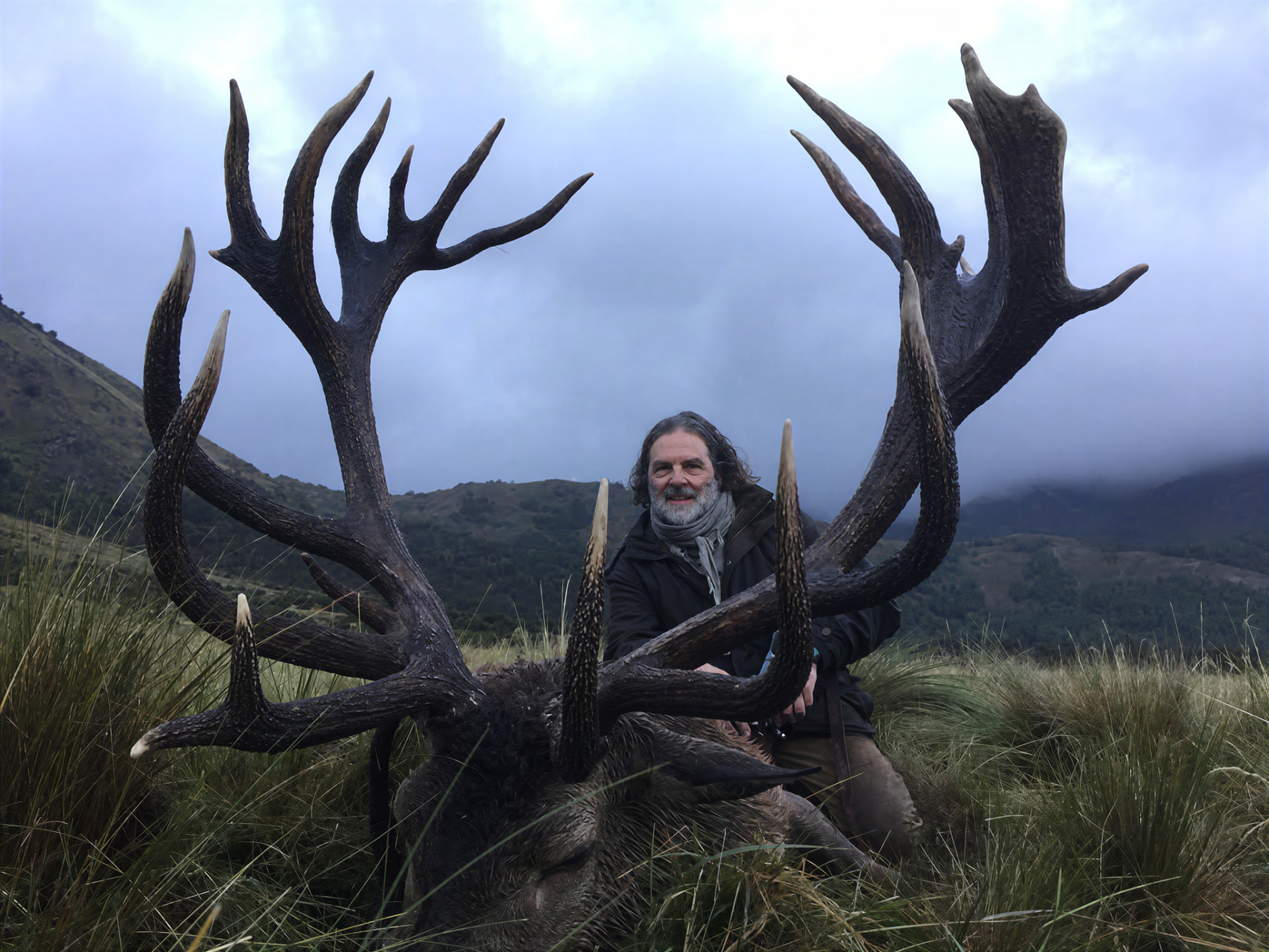 Hunter with a dark massive red stag under storm clouds