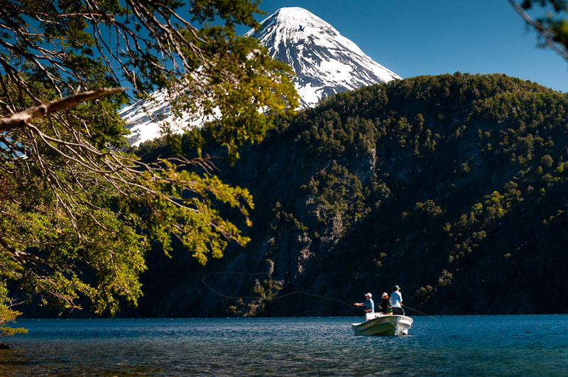 Anglers fly fishing from a boat on a Patagonian lake below the snow-capped Volcán Lanín