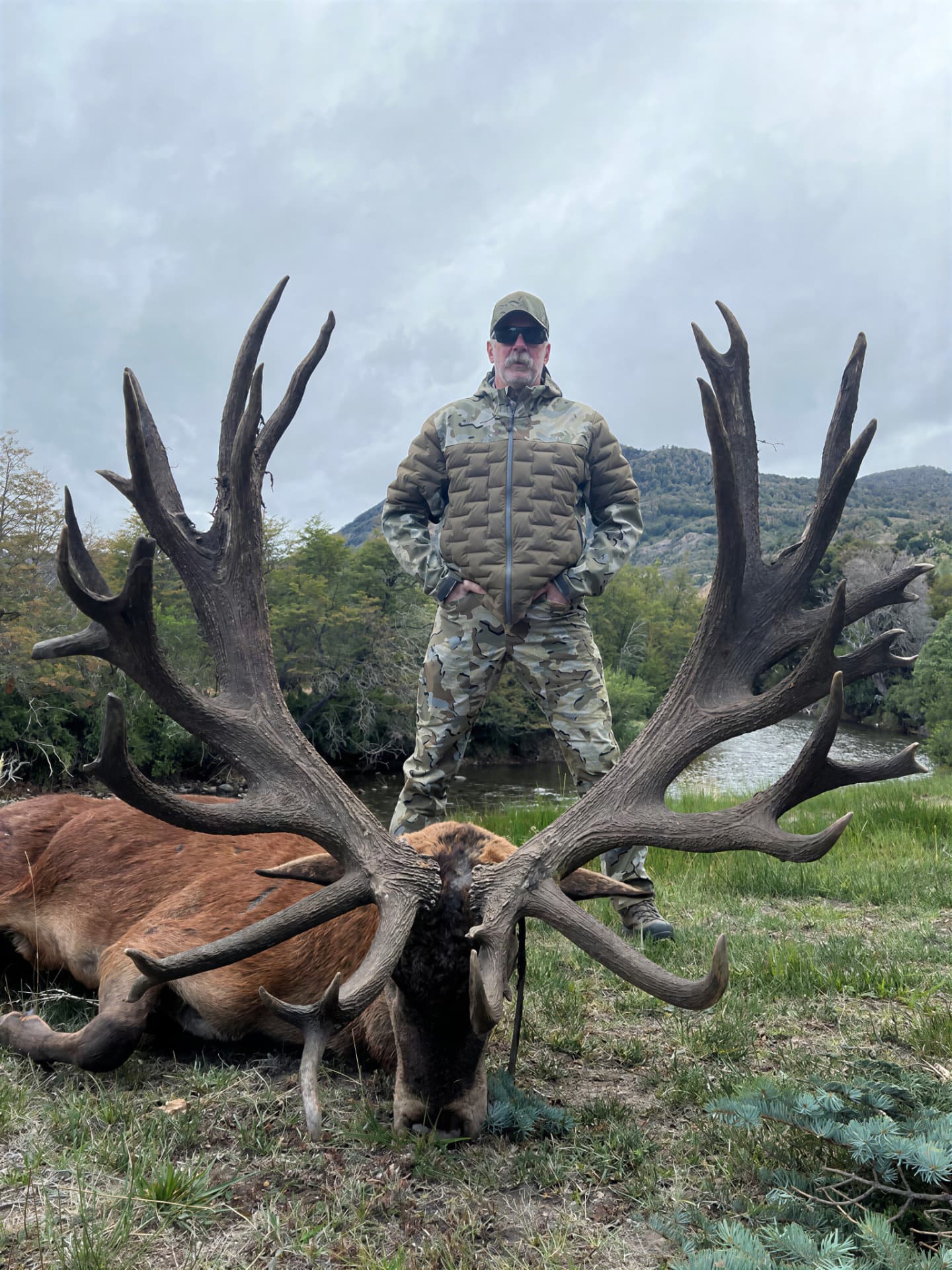 Hunter standing behind a massive red stag beside a Patagonian river