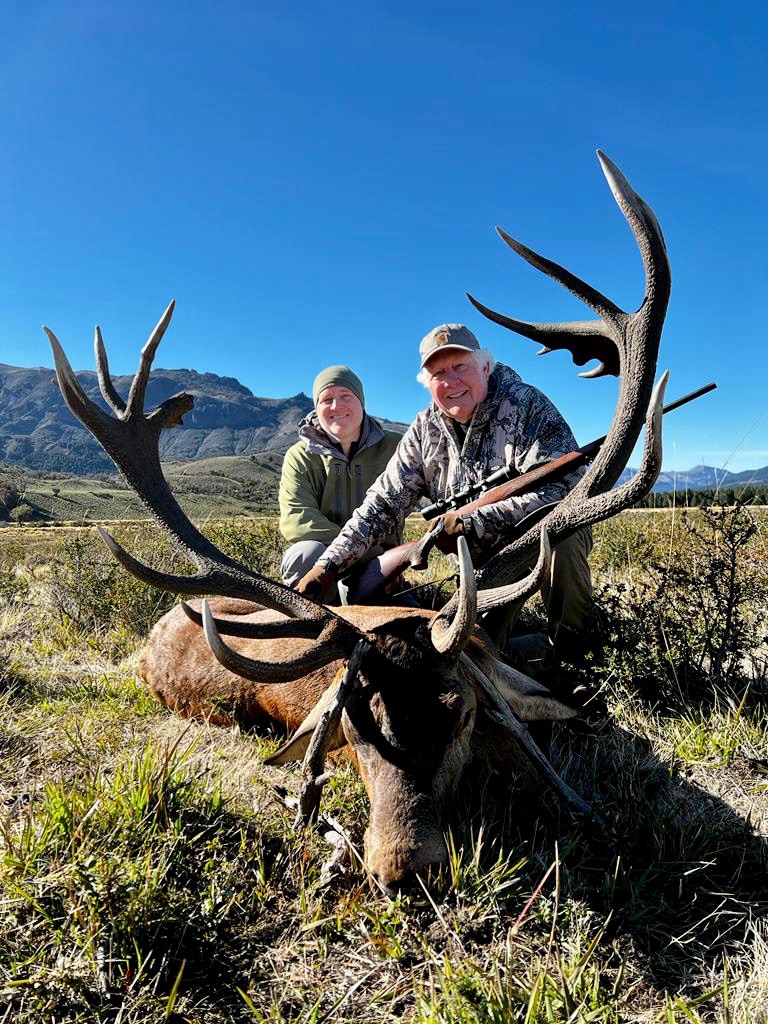 Two hunters with a wide red stag under clear Patagonian skies
