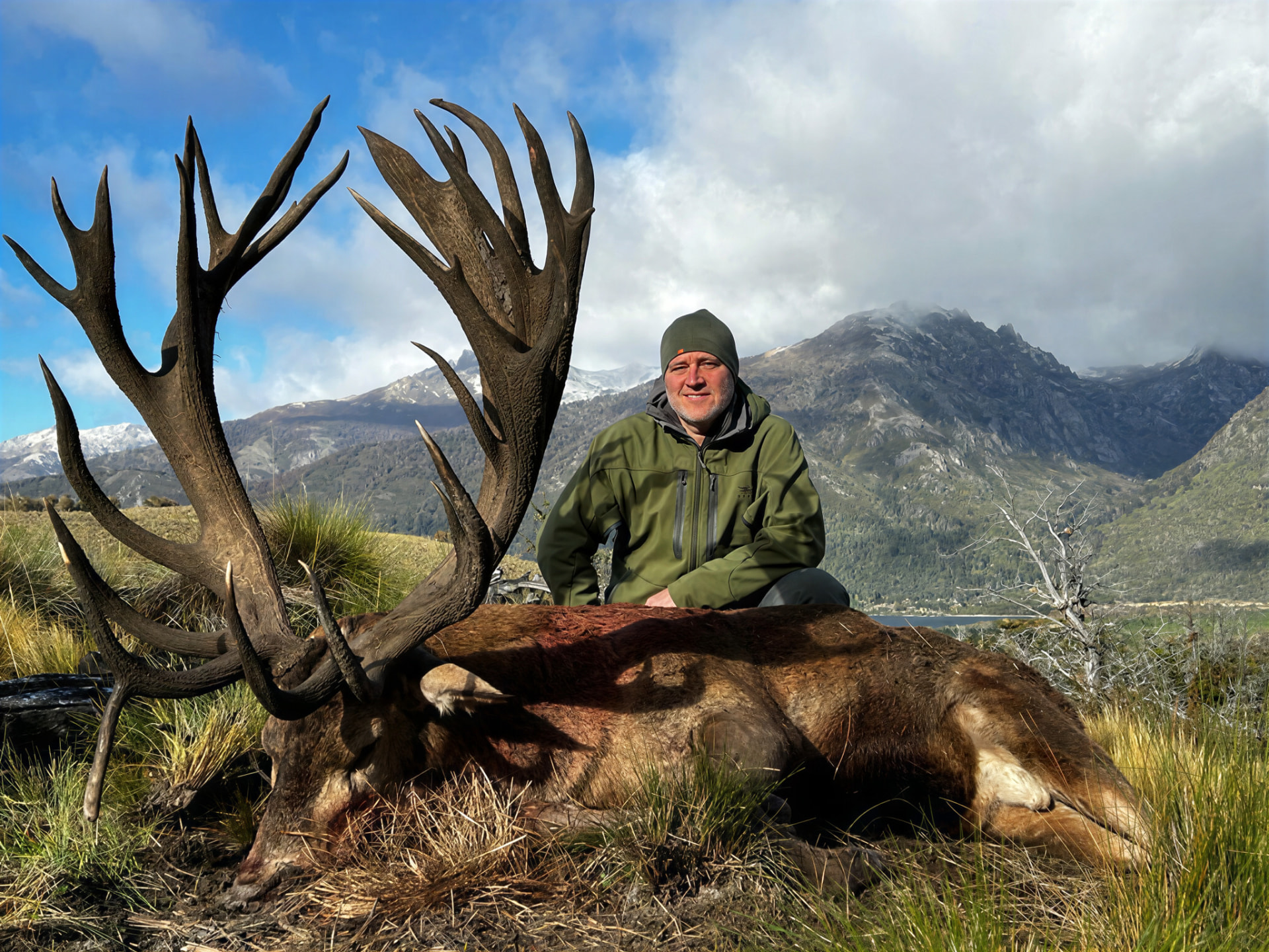 Hunter with a dark-antlered stag against snow-dusted mountains