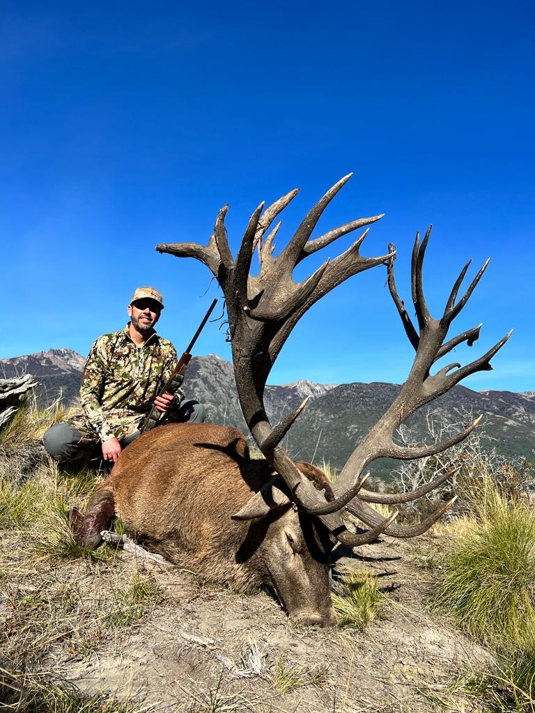 Hunter with a towering, heavily tined red stag on a mountain ridge