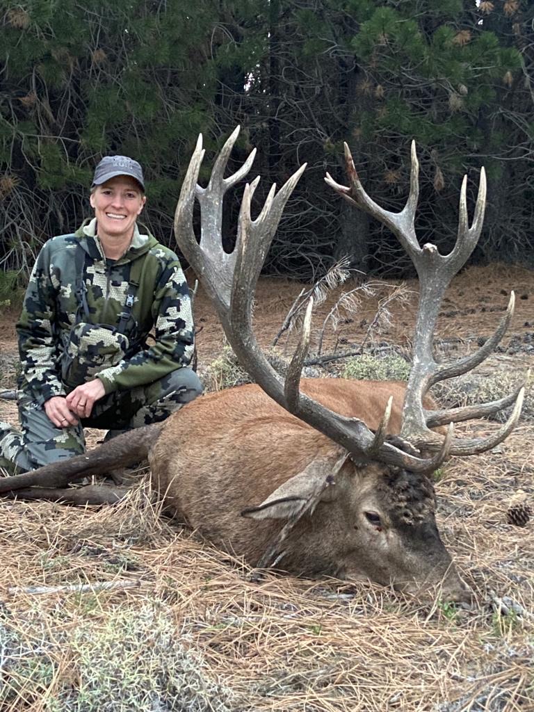 Lady hunter kneeling beside a mature red stag in the pines