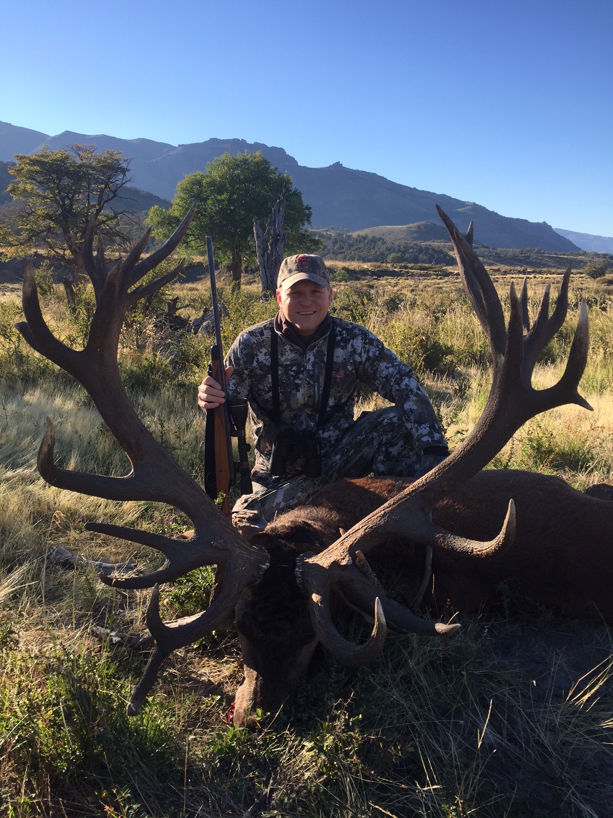 Hunter kneeling with a heavy multi-point red stag in golden grass