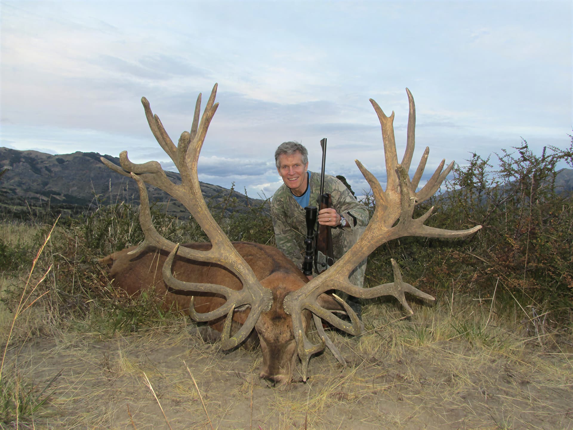 Hunter with rifle beside a heavy red stag on open Patagonian ground