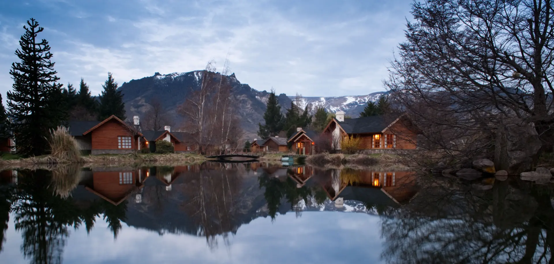 The cabins at Parque Diana reflected in the pond at dusk, Andes behind
