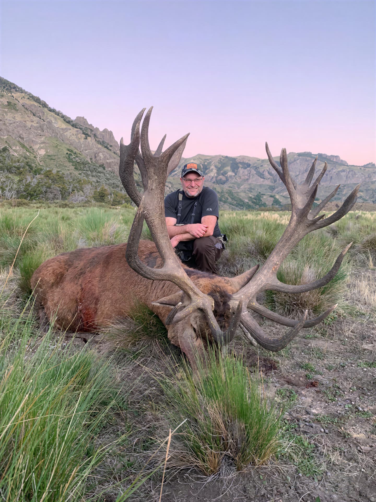 Hunter with a heavy gold-medal red stag in tussock grass at sunset