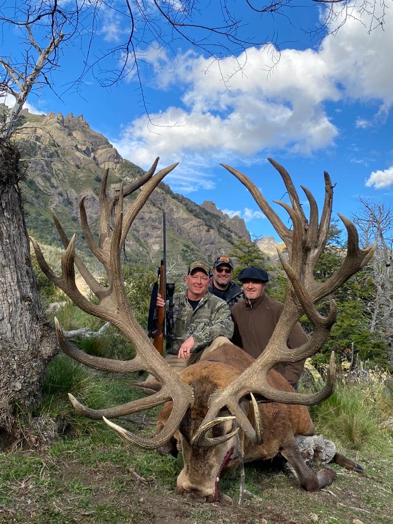 Three hunters behind a massive red stag below the Andean peaks