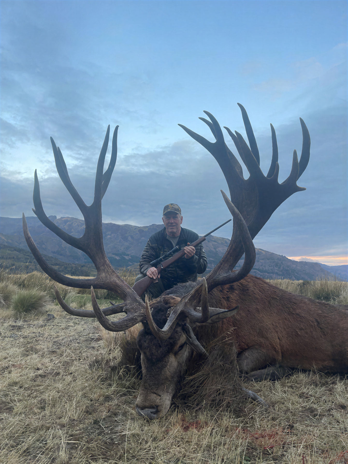 Hunter behind an enormous gold-medal red stag with massive multi-tined antlers in the Patagonian mountains