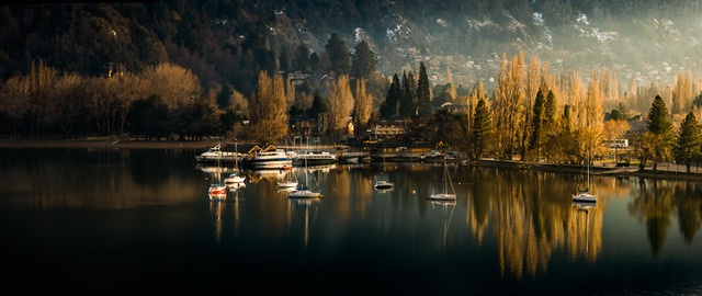 Sailboats moored on Lago Lácar at sunset with autumn poplars and forested mountains behind