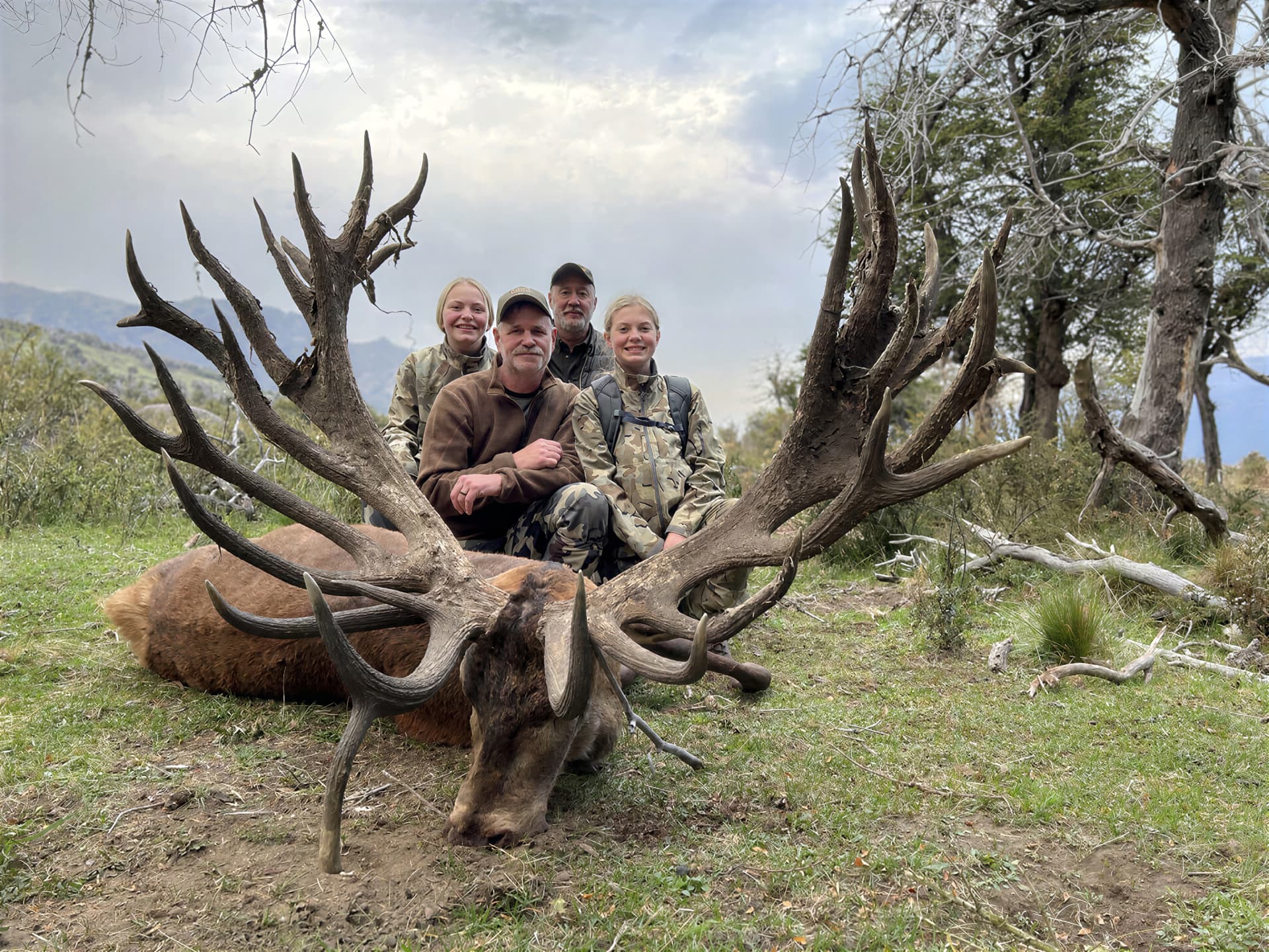 Family of hunters behind an enormous multi-tined gold-medal red stag in the Patagonian mountains