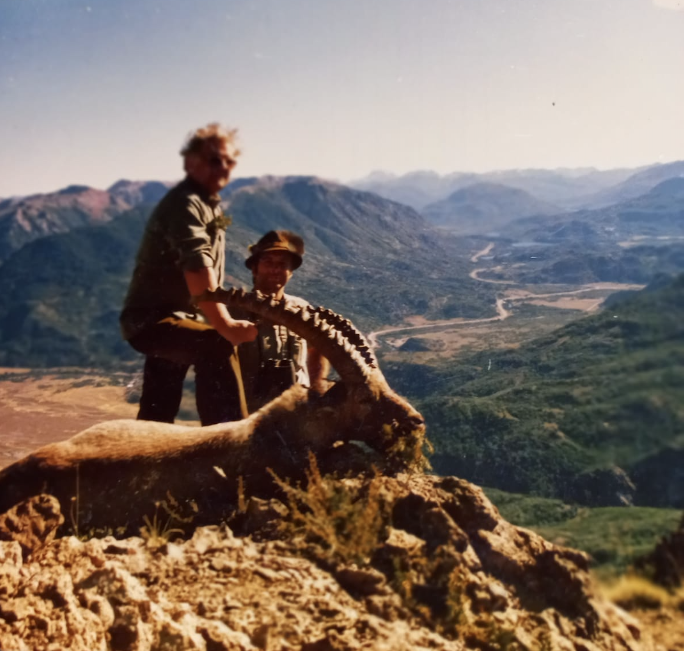 1983 archive photograph of head guide Beat Affolter and hunter Mr. März standing beside a mature Alpine ibex billy high above Parque Diana