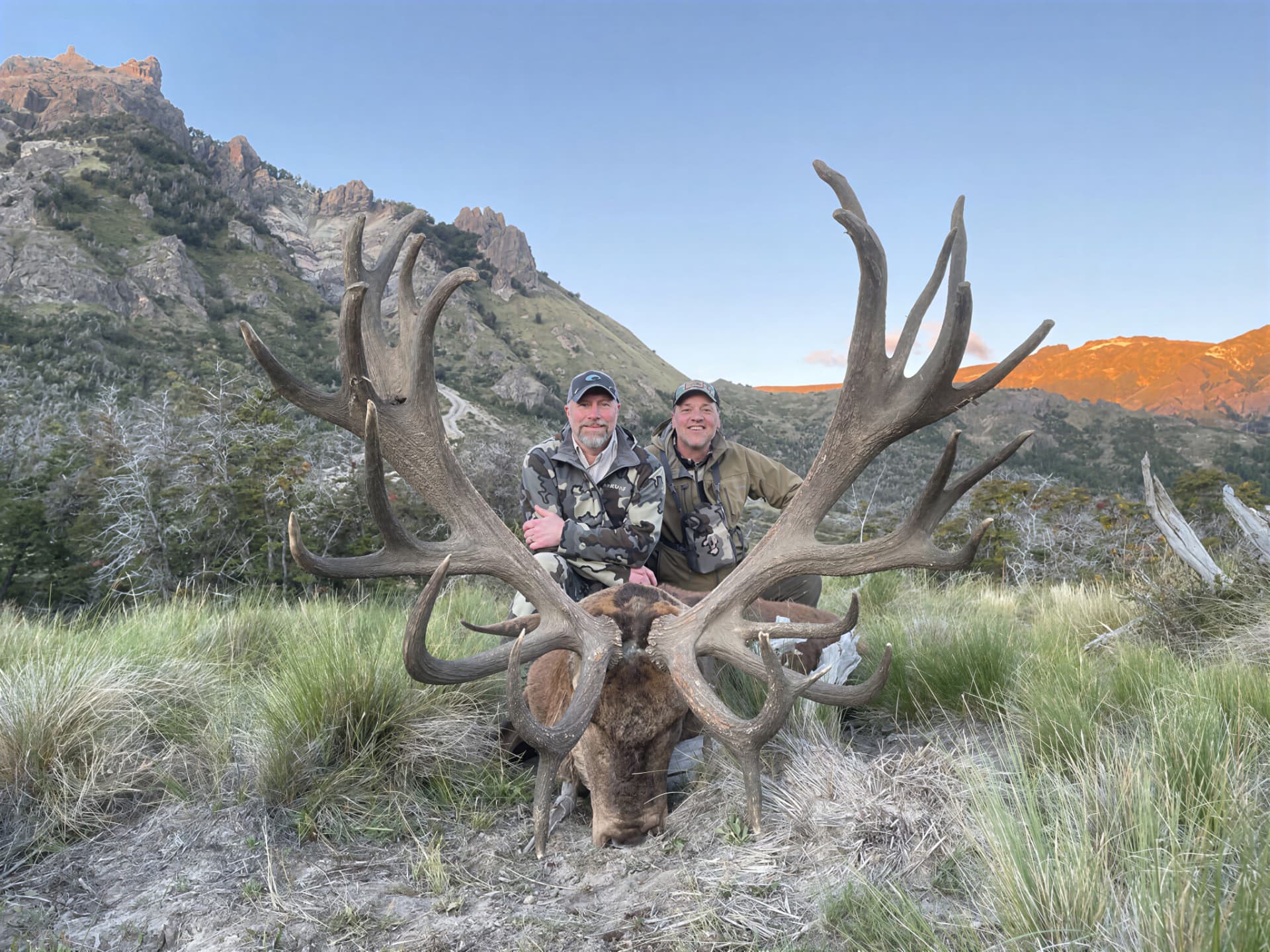 Two hunters with a gold-medal red stag at sunrise in the mountains