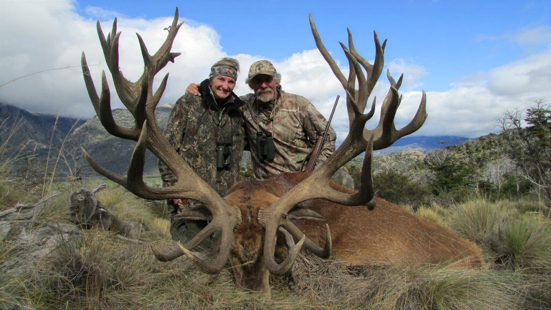 Two hunters with a heavy red stag against the Andes