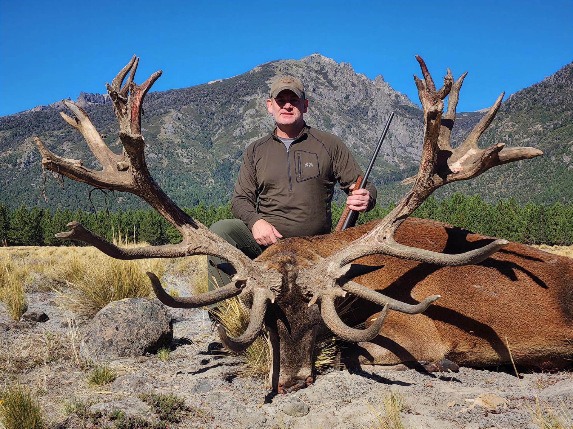 Hunter with a wide-antlered red stag against a mountain backdrop