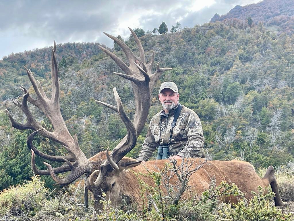 Hunter with a long-beamed red stag on a forested Andean slope