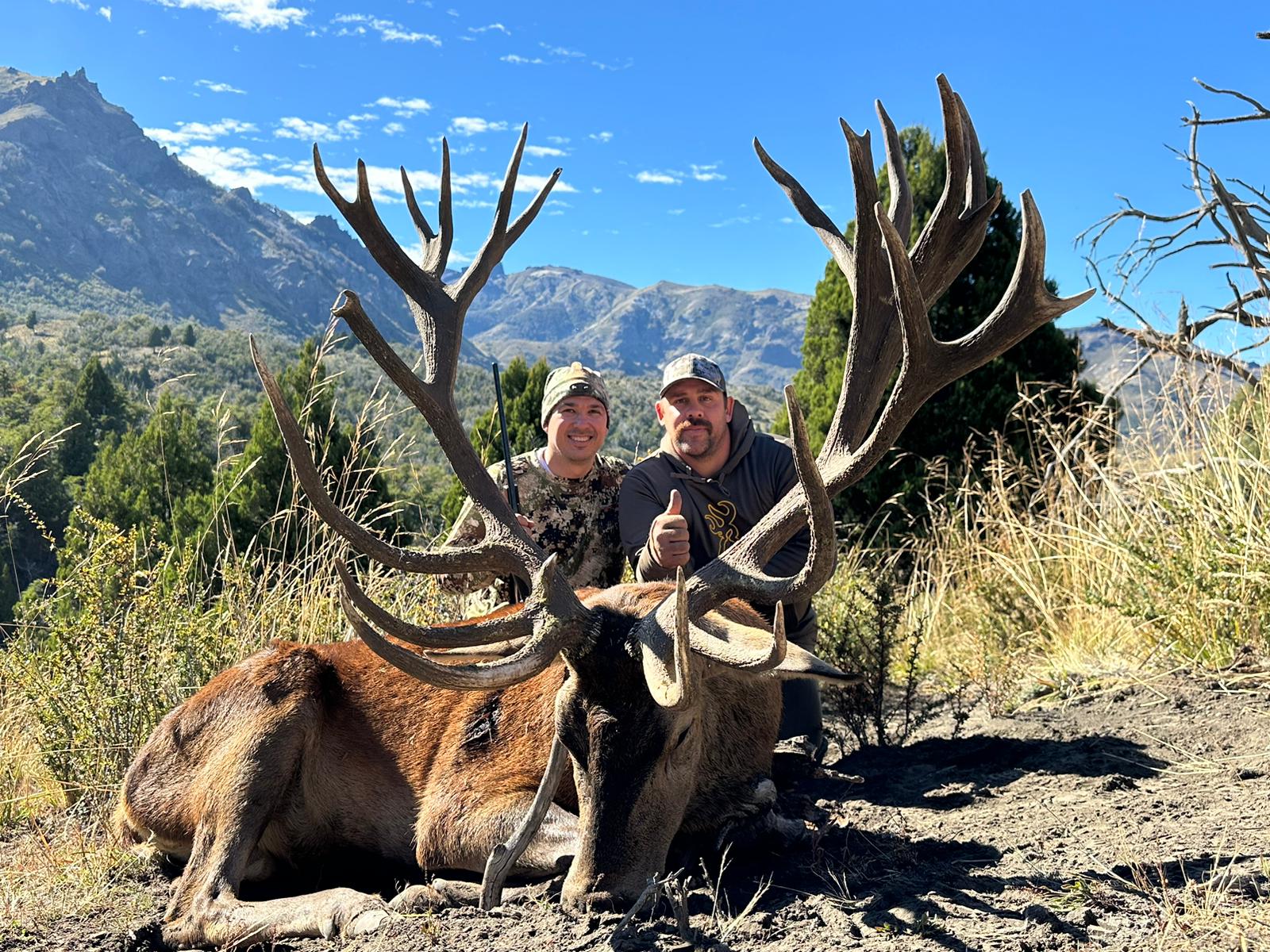 Two hunters with an exceptional heavy-beamed red stag below the Andean peaks
