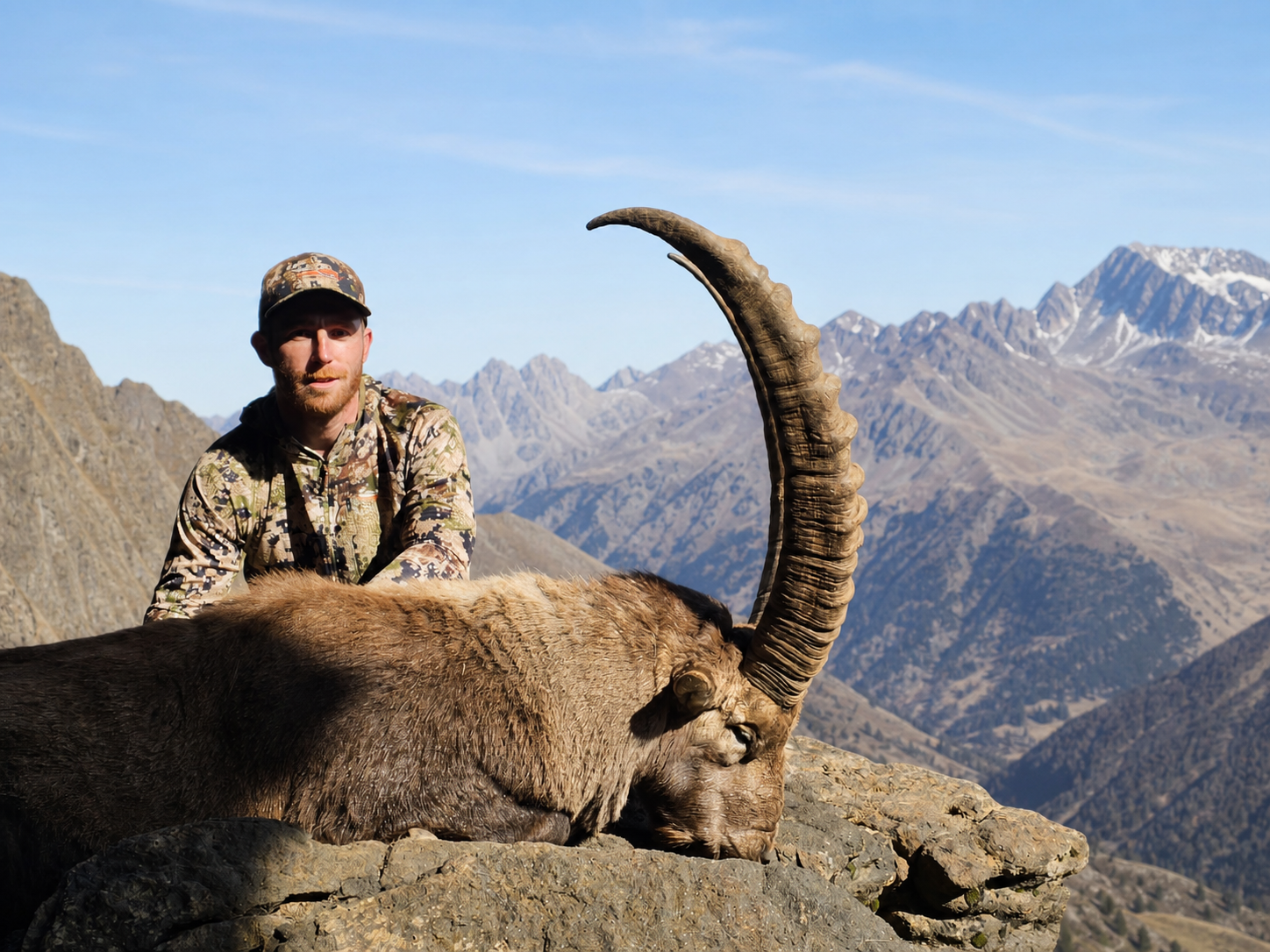 Hunter with a heavy, long-horned free-range Alpine ibex on a high rocky ridge