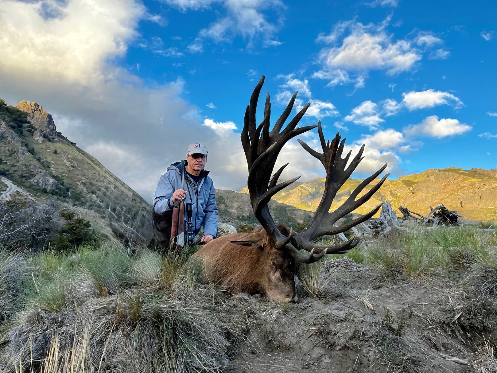 Hunter and dark-antlered red stag on a high mountain ridge